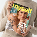 Person in beigem Strickpullover hält eine Ausgabe der Zeitschrift „myself“ mit gelb-weißem Logo und hellblauem Hintergrund. Auf dem Cover eine Frau mit goldenen Ohrringen und Kette, in weißem Top vor türkisfarbenem Hintergrund. Sichtbare Texte: „Mehr Zeit für mich“, „22 Urlaubs-Highlights“, „Relight my fire“, „Das Leben feiern“, „Schluss mit nett“, „Fast wie fliegen!“, „Haut ohne Hitzestress“.