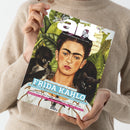 Person in beigefarbenem Strickpullover hält das Magazin „art – Das Kunstmagazin / Juli 2026“ in beiden Händen, Titelbild mit Porträt von Frida Kahlo vor grünem Blätterhintergrund und Tieren, Schriften in Weiß, Hellblau, Schwarz und Pink mit Themenzeilen zu Frida Kahlo, Raumpoetik, Vilhelm Hammershøi und Kreativität, fotografiert aus frontaler Perspektive vor neutralem Hintergrund.
