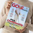 Person in beigem Strickpullover hält eine Ausgabe des „GOLF MAGAZIN“ mit Titel „PGA Championship“. Auf dem Cover steht ein männlicher Golfer in weißem Shirt, weißer Hose, weißer Kappe und Schuhen auf einem grünen Golfplatz vor blauem Himmel. Sichtbare Texte: „Sport“, „Rund um Wien“, „Training“, „Mega Event“, „Equipment“, sowie Unterzeile „Matti Schmid spielt ganz vorn mit – Aaron Rai gewinnt sein erstes Major“.