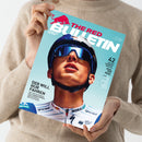 Titelblatt des Magazins „The Red Bulletin“ mit großem Nahporträt einer männlichen Person mit Fahrradhelm und verspiegelter Sonnenbrille vor hellblauem Hintergrund, sichtbare Texte u. a.: „DER WILL NUR FAHREN“, „BORA“, „grenke“, „UCI WORLD TEAM“, „42 SEITEN SOMMER-SPECIAL – FEEL THE REAL“, rotes Bullenkopf-Logo oben links. Gehalten von einer Person in beigem Strickpullover vor neutralem Hintergrund.