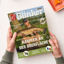 Titelbild der Angelzeitschrift „Blinker“ mit dem Untertitel „Europas große Angelzeitschrift“. In der Mitte hält eine männliche Person in Outdoor-Kleidung einen großen Karpfen vor grünem Hintergrund aus Gras und Bäumen. Textüberschriften: „Karpfen an der Oberfläche“, „Aale in Gräben“, „Urlauber aufgepasst!“, „Vänern-Hechte“, „Bergsee-Forellen“, sowie kleinere Hinweise zu „Juli-Schleien“ und Angelmethoden.