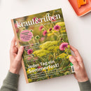 Titelblatt der Gartenzeitschrift „kraut&rüben“ Ausgabe 07/2026, gehalten von zwei Händen vor hellem Hintergrund. Coverfoto mit gelb blühendem Doldenblütler und rosa Wildblumen. Sichtbare Texte: „TOMATEN-LIEBE – Pflege-Leitfaden für köstliche Früchte“, „Jeder Tag ein Sommerfest!“, Themen zu griechischem Gemüse, Pflanzenkohle und Permakultur. Linke Kante mit braunem Heftstreifen und Zeitschriftentitel.