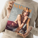 Magazincover der Zeitschrift „MADAME“ in orangefarbener Schrift auf grauem Hintergrund, gehalten von einer Person in beigem Strickpullover. Abgebildet ist eine Frau in bordeauxroter Spitzenbekleidung auf einem Holzstuhl. Text auf dem Cover: „SPECIAL REISE LUST“, „Japans schönste Gärten“, „Griechenland für Insider“, „Kopenhagen – Europas Stilmetropole“, „Beach Wear & Accessoires mit Ocean Flair“.