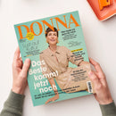 Titelblatt der Zeitschrift „DONNA“ mit türkisfarbenem Hintergrund und orangem Schriftzug oben. In der Mitte eine lächelnde Frau mit kurzen braunen Haaren, beigefarbener Hemdbluse und schimmerndem Rock, sitzend dargestellt. Sichtbare Texte u. a.: „Das Beste kommt jetzt noch“, „Lust auf Kultur“, „Hier bade ich ganz für mich“, sowie Rubriken zu Frisur, Hormonen und Kultur. Zwei Hände halten das Magazin über hellem Untergrund.