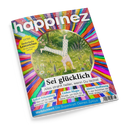 Titelbild des Magazins „Happinez“ mit farbenfrohem, regenbogenartigem Hintergrund und einer Illustration einer Person, die im Gras einen Handstand macht. Hauptüberschrift: „Sei glücklich – Alles strahlt heller, wenn Du lachst“. Weitere Textelemente: „Selbst-Erkenntnis“, „Liebes-Magie“, „Aktive Hoffnung“, „Weiblichkeit – Die Superkraft Deines Zyklus“ und Hinweis auf ein „Extra Zauberhaftes Lesezeichen“.