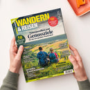 Titelblatt des Magazins „Wandern & Reisen“ mit sommerlicher Landschaft im Hintergrund. Zwei Personen von hinten, eine mit blauem Rucksack, eine mit Hut und pinker Jacke, sitzen auf einer Wiese und blicken auf ein Tal mit Feldern und Dörfern. Überschriften u. a.: „Naturparadiese und Genussziele“, „Ratgeber: Blasen verhindern“, „Premium-Wanderwelten“ und „50 frische Ideen für einmalige Sommertouren“.