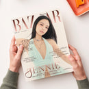 Titelblatt der Zeitschrift „Harper’s Bazaar“ Ausgabe 05/06 2025, gehalten von zwei Händen über einem hellen Tisch mit orangefarbener Schale. Auf dem Cover eine weibliche Person mit langen dunklen Haaren in mintgrünem, tief ausgeschnittenem Kleid, silberner Halskette und neutralem Gesichtsausdruck. Sichtbare Texte: „DER BAZAAR SMART GUIDE“, „HOSENANZÜGE AUFREGEND ANDERS“, „THE GREAT OUTDOORS“, „JENNIE – EXKLUSIV: DER BLACKPINK-STAR“.