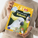 Eine Person in beigefarbenem Pullover hält das Kinderheft „GEOlino mini“ mit gelbem Titelrand und großem Foto eines weißen Kakadus mit gelbem Federschopf vor grünem Hintergrund; Aufschriften: „Schick und schrill: Kakadu“, „WISSEN – Was die Wolken über das Wetter verraten“, „Suchen – Erkunde die Puppenstube“, „Kinder: Kylian gräbt eine Burg aus“, illustriertes Leopardenkind unten rechts, geeignet ab 5 Jahren.