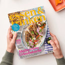 Magazin „essen & trinken“ mit gelbem Titel auf hellblauem Hintergrund, gehalten von zwei Händen über einer weißen Tischfläche; Titelbild zeigt Teller mit mediterranem Gericht aus gegrillten Spießen, Zwiebeln, Kräutern, Paprika und Käsekrümeln, daneben kleiner Teller mit Oliven und Zitronenstücken auf blau-weiß gestreiftem Tuch, Schriftzüge u. a. „Mediterrane Urlaubsküche“ und „Saucen-Schule 2. Teil: Von Aioli bis BBQ“.