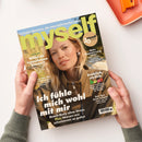 Titelbild der Zeitschrift „myself“ mit hellgrünem Logo, goldfarbenem Schriftzug „20 Jahre“ und einer weiblichen Person mit langen blonden Haaren in brauner Jacke vor unscharfem Hintergrund. Text auf dem Cover: „Ich fühle mich wohl mit mir“, „Willst du irgendwann Kinder?“, „Mehr Begeisterung, bitte!“, „Fröhlich, stylish, bunt“, „Den Sex ihres Lebens“ sowie kleinere Unterzeilen in Weiß, Gelb und Grün. Hände halten das Magazin über hellem Tisch.