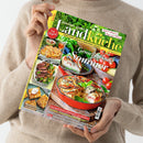 Eine Person in beigem Strickpullover hält die Zeitschrift „meine gute Landküche“ in beiden Händen; Titel mit grün-gelbem Layout und Bildern von sommerlichen Gerichten, darunter Gemüse-Quiche, Steaks, Focaccia und Kuchen. Sichtbare Texte: „Genießen im Sommer“, „Hausgemacht schmeckt’s am besten!“, „Frisch gebacken: von Focaccia bis Zupfbrot“, „Schnelle Kuchen mit Sommerfrüchten“, Ausgabe Juli/August 2024.