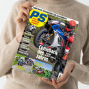 Person mit hellbeigem Strickpullover hält das Motorradmagazin „PS sport motorrad magazin“ in beiden Händen, Titelaufschrift „Comeback des Jahres – Suzuki GSX-R 1000 R“, großes Titelbild zeigt eine Person in roter Motorradausrüstung auf blauer und weißer Suzuki. Weitere sichtbare Textthemen: „Vergleich Superbikes“, „Vergleich Naked Bikes“, „Premiere Norton Manx R“, „TunerGP“, „Hausstrecke Bimota KB4 RC“.