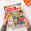 Titelblatt der Zeitschrift „selber machen! DIY – Bauen, Gestalten, Renovieren“, Ausgabe Juli 2020, gehalten von zwei Händen über hellem Tisch. Im Zentrum ein foto eines männlichen Erwachsenen, der mit einem Akkuschrauber ein Holzgestell baut, daneben Überschriften wie „MÜLLTONNEN VERSTECKEN“, „Klassisch aus Holz“, „Schweben wie auf Wolken“ und Themensegmente zu Werkzeugen, Terrassenbau und Gartenideen.