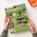 Titelbild der Zeitschrift „LandIDEE – Land erleben und genießen“, Ausgabe Juli & August 2024. Auf dem Cover: eine grüne Wiesenlandschaft mit Holzfässern als Mini-Teiche, bunten Blumen und Kräutern. Sichtbare Texte u. a.: „153 Ideen für den Sommer“, „Zauberhafte Sonnentage“, „Neue Einmach-Ideen für Obst & Gemüse“, „Gesunde Hausmittel mit Kamille“. Gehaltene Hände einer Person in grünem Strickpullover vor hellem Hintergrund.