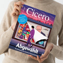 Titelbild des Magazins „Cicero – Magazin für politische Kultur“, gehalten von einer Person in beigefarbenem Strickpullover. Das Cover zeigt eine Illustration mit einer Figur im lila Anzug, die ein Plakat mit Parteilogos wie CDU, SPD, FDP, AfD und Die Linke abzieht. Oben pink-violetter Himmel mit Stadtsilhouette, blaue Rundmarke „Sendestörung – Die wahren Probleme des öffentlich-rechtlichen Rundfunks“, Überschrift „Abgewählt – Der Untergang des deutschen Parteiensystems“.