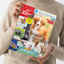 Person in beigem Strickpullover hält das Magazin „Ein Herz für Tiere“ vor neutralem Hintergrund; auf dem Titel ein braun-weißer Hundewelpe mit der Aufschrift „Mit dir ist immer Urlaub!“, daneben kleinere Fotos von Kaninchen, Dachs, Fisch und Luchs sowie Textzeilen wie „Freundschaften“, „Wildtiere“, „Party­motto Lieblingstier“ und Hinweis „Schmetterlinge – Geheimnisse der elfenhaften Wesen“.