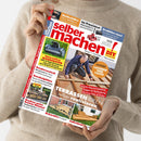 Person mit hellbeigem Strickpullover hält ein Exemplar der DIY-Zeitschrift „selber machen!“ mit rotem Logo und gelbem Zusatz „Do it yourself“. Auf dem Titel sind ein Mann beim Bau einer Holzterrasse, mehrere kleinere Bilder von Holzprojekten, Werkzeugen und Gartenideen zu sehen. Schlagworte: „TERRASSEN-IDEEN selber realisieren“, „LASUREN UND LACKE“, „Innovative Mähroboter“, „Kuschelplätze“ und „Kochen unter freiem Himmel“.