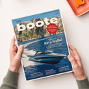 Titelblatt des Magazins „boote“, Ausgabe 7/2026, gehalten von zwei Händen über einer hellen Tischfläche. Auf dem Cover ein Foto einer blaugrauen Motoryacht auf dem Wasser vor Felsenküste. Hauptüberschriften: „Großer Test Riva Italia!“, „Gebrauchtboote“, „Niederlande“, „Seemannschaft“. Roter Kreis mit Text „Tipps für den Motor-Check“. Hintergrundfarben in Blau- und Beigetönen, klar strukturierte Schriftgestaltung.