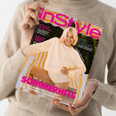 Person in beigefarbenem Strickpullover hält eine Ausgabe des Magazins „InStyle“. Das Cover zeigt eine blonde weibliche Person in hellem Pullover und Shorts auf einer gestreiften gelb-weißen Liege. Magentafarbener Schriftzug „InStyle“ im oberen Bereich, Texte u. a.: „ACCESSOIRES FÜR HEISSE TAGE“, „PALM BEACH, SCHWEDEN, FLORENZ“, „EASY GLOWING“ und „SOMMERHITS – POLKA DOTS ALLOVER, WEISSE JEANS, SÜSSE SPITZEN-SHORTS, COOLE BASEBALL-SHIRTS“.