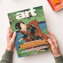 Schräg liegendes Kunstmagazin aus Papier mit grünem Cover, japanischer Farbholzschnitt-Darstellung einer weiblichen Person im farbenreichen Kimono vor Wasser und Pflanzen; zwei Hände halten das Magazin. Sichtbare Texte: „art“, „DAS KUNSTMAGAZIN // AUGUST 2026“, „JAPANLIEBE“, „MIT POSTER-EDITION ZUM HERAUSNEHMEN!“, „MANIFESTA 16 RUHR“ und „PAUL SIGNAC IN POTSDAM“.