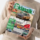 Diagonal gehaltenes Magazin „Auto Bild Klassik“ in den Händen einer Person mit beigefarbenem Strickpullover. Das Cover zeigt einen alten Mercedes vor einer kargen Landschaft, die Aufschriften „W123 Challenge“, „Die Jagd auf W123“, „Lastentier mit Leidenschaft“, „Im alten Benz quer durch Marokko“ und „Klassiker bis 10.000 Euro“ sowie weitere Oldtimer-Abbildungen und eine marokkanische Flagge.