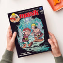 Comic-Heft mit dem Titel „Mosaik“ in roter Schrift, Ausgabe 607 Juli 2026, Untertitel „Abenteuer in der goldenen Stadt“ und Episodentitel „Tumult auf dem Hradschin“. Auf dem Cover drei gezeichnete Figuren mit mittelalterlicher Kleidung in einem nächtlichen Wald mit Mondlicht; oben links runde Illustration der gleichen Figuren; Heft wird von zwei Händen über hellem Hintergrund gehalten.