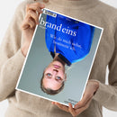 Aufgeschlagene Ausgabe des Magazins „brand eins“ mit blauem Titelbild und dem Text „Das geht!“ sowie „Wie du mich siehst, bestimme ich.“ Eine weibliche Person mit hellbeigem Strickpullover hält das Magazin schräg vor dem Körper; auf dem Titel ist eine Frau mit blauem Oberteil abgebildet.