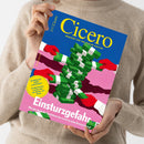 Hochformatiges, schräg gehaltenes Magazin „Cicero – Magazin für politische Kultur“ in den Händen einer Person mit beigefarbenem Strickpullover. Das Cover zeigt rote Handschuhe und einen Stapel grüner 100-Euro-Scheine vor blau-pinkem Hintergrund; lesbare Texte: „SEHNSUCHT ODER ALBTRAUM? Großbritannien streitet über die Abkehr vom Brexit“, „Einsturzgefahr“ und „Wie der deutsche Sozialstaat das Land an seine Grenzen bringt“.