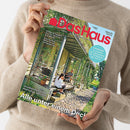 Weibliche Person im beigefarbenen Strickpullover hält ein schräg fotografiertes Magazin mit dem roten Titel „DAS haus“ und der Zeile „BAUEN • WOHNEN • SCHÖNER LEBEN“. Das Cover zeigt ein begrüntes Gewächshaus sowie die Texte „Farben & Tapeten“, „Solartechnik“, „Naturgarten“ und „Großfamilie saniert ehemalige Spinnerei – Alle unter einem Dach“.