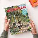 Zeitschrift „Das Haus“ mit rotem Titel und dem Untertitel „Bauen, Wohnen, schöner leben“, auf einem Gewächshausfoto mit Pflanzen, einer sitzenden erwachsenen Person und einer weiteren Person mit Kind. Sichtbare Texte: „Naturgarten: So schaffen Sie Lebensräume für Wildbienen, Igel und Co.“, „Farben & Tapeten: Frischer Wind für Ihre Wände“, „Solartechnik: Bereit für die Sonnenwende“ sowie „Großfamilie saniert ehemalige Spinnerei“ und „Alle unter einem Dach“.