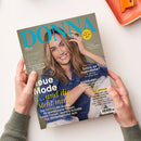 Aufgeschlagen gehaltene DONNA-Zeitschrift mit braunhaariger weiblicher Person im blauen Jeanshemd auf dem Cover, gelbem Kreis „Meine Zeit ist jetzt“ und Texten wie „Lesen, lachen, abtauchen“, „Zurück zur Jugendliebe?“ sowie „Andalusien“. Zwei Hände halten das Magazin über einer weißen Fläche; oben rechts liegen ein orangefarbenes Heftgerät und ein orangefarbenes Notizbuch.