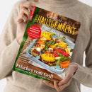 Weibliche Person im beigefarbenen Strickpullover hält ein schräg fotografiertes Magazin mit dem Titel „LandLust HAUSGEMACHT“, Untertitel „Mein Magazin für Haus und Küche“. Das Cover zeigt gegrilltes Gemüse und Fleisch sowie die Texte „Eis selber machen“, „Schnelles für heiße Tage“, „Marmeladen“, „Gegrillte Fladenbrote“ und „Frisches vom Grill“.