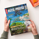 Magazin „Reise und Preise“ mit dem Titelbild einer Küstenlandschaft mit türkisblauem Meer, weißer Steilküste, grünem Bewuchs und Sonnenschirmen am Strand, gehalten von zwei hellhäutigen Händen über hellem Tisch; Aufschrift u. a.: „Queensland – Australiens Naturwunder“, „Den Sommer verlängern“, „19 traumhafte Ziele für die Nebensaison“, sowie Themen Istrien, Bangkok, Irland und Marokko.