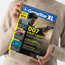 Person in beigem Strickpullover hält das Magazin „GameStar XL“ in beiden Händen, Cover mit blau-gelbem Layout. Hauptmotiv ist ein Mann mit Pistole in Nahaufnahme. Titelüberschriften: „007 First Light – Die Hitman-Macher schicken uns in ein geniales James-Bond-Actionspiel“, dazu Berichte zu „Assassin’s Creed: Black Flag Resynced“, „Forza Horizon 6“, „New Cycle“, „Paradise Killer“ und „Verne“.
