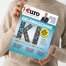 Beigefarben gekleidete Person hält das Magazin „€uro – Das Magazin für Wirtschaft und Geld“, Ausgabe 7/2026. Titel in Großbuchstaben: „GELDMASCHINE KI“, Schrift mit goldfarbenen Leiterbahnen und blauen Mikrochip-Elementen gestaltet. Gelber Kreis mit Text „Der große Praxis-Test“, weitere sichtbare Texte: Themen zu KI-Fonds, Aktien, Dividenden, Börsengängen und Fonds; Hintergrund in Hellblau mit technischem Platinenmuster.