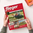 Rot gerahmtes Magazin „flieger MAGAZIN“ in leichter Vogelperspektive, von zwei Händen gehalten. Das Cover zeigt ein Kleinflugzeug mit „FOR SALE“-Schildern sowie weitere Flugzeuge und ein Cockpit; sichtbare Texte: „Was ein Flugzeug wirklich kostet“, „Tipps für Kauf & Betrieb“, „Gebrauchtflugzeuge“, „5 Flugzeug-Porträts: Cessna, Piper & Co.“ und „Einsteiger-Gebrauchtflugzeuge · Haltergemeinschaft · Geheimtipps · Finanzierung“.