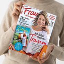 Eine Person im beigefarbenen Strickpullover hält ein schräg fotografiertes Magazin mit glänzendem Papier. Das Cover von „Frau im Leben“ zeigt eine lächelnde blonde Frau und die Texte „Die 5-Euro-Küche“, „10 Ideen für kleine Räume“, „Neue Mode“, „Ich liebe meinen Mann“ sowie „Bayern für Entdecker“.