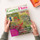 Von zwei Händen gehaltene Zeitschrift „GartenFlora“ mit dem Untertitel „gärtnern, erleben und genießen“, Ausgabe September 2026. Das Cover zeigt einen farbenreichen Garten mit Blumen und Gräsern, ein Foto einer weiblichen Person sowie die Texte „Biozüchtergarten: So werden Sommerblumen gezüchtet“, „Magischer Spätsommer in Burgund“ und „Mini-Kiwis für den Garten“; oben rechts liegt ein oranges rechteckiges Objekt.