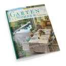 Schräg fotografierte Zeitschrift mit türkis-grünem Rand und dem Titel „GARTEN WOHNEN Träume“. Das Cover zeigt eine begrünte Terrasse mit Pool, gedecktem Esstisch, Korbstühlen, Pflanzen und einem Essbereich im Hintergrund; sichtbar sind außerdem die Texte „Genießen wie im sonnigen Süden“, „Cloud Dancer“, „Lavendelfeldern“ und „Wasserbecken“.