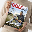 Schräg gehaltenes Magazin „GOLF MAGAZIN“ mit weißem Cover, roter Titelzeile und dem Datum „September 2026“, in zwei Händen vor einem beigefarbenen Strickpullover. Das Cover zeigt einen Mann im schwarzen Poloshirt mit silberner Trophäe sowie die Texte „Profilgolf“, „Vorschau: Solheim Cup“, „BMW International Open“, „German Challenge“, „The Open 2026“, „Ryan Fox“ und „Der erste Major-Sieg des Neuseeländers“.