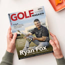 Schräg fotografiertes Cover des „GOLF MAGAZIN“, September 2026, auf weißer Fläche, von zwei Händen mit grauen Strickärmeln gehalten; oben rechts liegt ein orangefarbenes Notizbuch mit Klammer. Das Cover zeigt eine männliche Person mit dunklem Poloshirt, die eine silberne Trophäe hält, sowie die Texte „Ryan Fox“, „Der erste Major-Sieg des Neuseeländers“, „Profigolf“, „Vorschau: Solheim Cup“, „BMW International Open“, „German Challenge“, „Reise“ und „Training“.