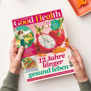 Schräg von oben fotografierte Zeitschrift „Good Health“ in den Händen einer Person, mit pinkem Cover, großer weiß-gelber Titelzeile und Abbildungen von Drachenfrüchten, Sanddorn sowie einem Brokkoligericht. Auf dem Cover sind eine weibliche Person und die Texte „Endlich schmerzfrei!“, „Japan-Workout“, „12 Jahre länger gesund leben“ und „Kraftpaket Brokkoli“ erkennbar.