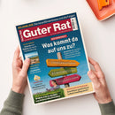 Diagonal auf einer weißen Fläche liegendes Magazin „Guter Rat“ mit blau-rotem Titelbild, von zwei Händen einer nicht näher bestimmbaren Person gehalten; oben rechts liegt teilweise ein orangefarbenes Kunststofftablett. Sichtbare Texte: „GELDANLAGE – Die neue Börsenblase und die Folgen“, „REFORMPAKET – Was kommt da auf uns zu?“, „Steuerreform“, „Rentenreform“, „Pflegereform“ sowie Hinweise zu Digitalwährung, Urlaubszielen, Eiscreme, Heckenscheren und Wärmepumpenförderung.