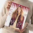 Weibliche Person in beigefarbenem, geripptem Strickpullover hält ein schräg zur Kamera ausgerichtetes, glänzendes Magazin mit beiden Händen. Das Cover zeigt eine Frau mit langem, welligem hellbraunem Haar und trägt die Texte „BAZAAR“, „Harper’s Bazaar“, „PFLICHTLEKTÜRE SMART IST DAS NEUE SEXY“, „IM INTERVIEW ROSALIA ÜBER EUPHORIE“, „EINE ODE AN VENEDIG“ und „DAS BESTE AUS DEN NEUEN KOLLEKTIONEN“.