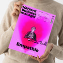 Eine Person im beigefarbenen Strickpullover hält ein schräg fotografiertes, pink-magenta-farbenes Magazin. Auf dem Cover stehen „Das Wissen der Besten“, „Harvard Businessmanager“, „Empathie“ und „Die Superkraft in der Krise“; abgebildet ist eine gezeichnete Person im Anzug, daneben das HBR-Logo sowie die Texte „Preissenkungen“, „Stakeholder Vertrauen aufbauen in Krisenzeiten“, „Einsteigerjobs“ und „Überlastung“.
