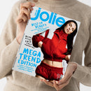 Schräg gehaltenes Magazin „Jolie“ mit blauem „Jolie“-Logo und den Texten „BEST OF BEAUTY“, „New-Season-Make-up“, „Die neuen Blond-Töne“, „Düfte, die nicht jeder hat“, „MEHR GELD ABER EASY“, „10 geniale Tipps“ sowie „MEGA TREND EDITION“. Auf dem Cover eine weibliche Person mit langen dunklen Haaren in roter Jacke und roter Hose; das Magazin wird von zwei Händen vor einem beigefarbenen Strickpullover gehalten.