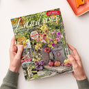 Hochformatiges, schräg gehaltenes Magazin „Landidee“ mit Gartenmotiv, bunten Blumen, Äpfeln und Dekoration aus Naturmaterialien; zwei Hände einer nicht näher bestimmbaren Person halten es am unteren Rand. Sichtbare Texte: „Land erleben und genießen“, „137 Ideen zum Selbermachen“, „Leckere Rezepte mit Äpfeln und Quitten“, „Herbstliche Deko für den Balkon mit Pflanzen“, „Bastelideen für unsere Gartentiere“ und „Leuchtfeuer für die Sinne“.