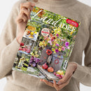 Weibliche Person im beigefarbenen Strickpullover hält ein schräg fotografiertes Magazin mit dem Titel „Landidee“. Das Cover zeigt einen blühenden Garten sowie Bilder mit Apfelkuchen, Granatäpfeln und Bastelideen; sichtbare Texte: „September & Oktober 2026“, „137 IDEEN ZUM SELBERMACHEN“, „Leckere Rezepte mit Äpfeln und Quitten“, „Herbstliche Deko für den Balkon mit Pflanzplänen“ und „Bastelideen für unsere Gartentiere“.