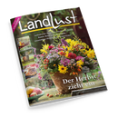 Schräg dargestelltes „Landlust“-Magazin mit schwarzem Hintergrund und großem Titel in Weiß. Das Cover zeigt einen üppigen Herbstblumenstrauß in einem rustikalen Gefäß, Äpfel, Hagebutten und Nüsse auf einem Holztisch sowie kleine Bilder eines Hirsches und herbstlicher Motive; lesbare Texte: „NEUE STRICKIDEEN“, „Laubsammler: Aufsatz für Schubkarren bauen“, „Basteln: Blüten aus Kleeblättern“ und „Der Herbst zieht ein“.