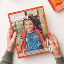 Rot gerahmtes Elternmagazin „leben & erziehen – DAS ELTERN-MAGAZIN“, diagonal von zwei Händen gehalten. Das Titelbild zeigt ein lächelndes Kind mit braunem Haar, blauem Latzkleid, gestreiftem Shirt und rotem Rucksack; lesbare Texte: „Reise nach Marokko“, „Familienfrieden“, „Selbstfürsorge“, „Aufs Bauchgefühl hören“ und „Halt in der Schule“. unerquicklich